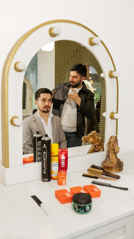 Ayna önünde damat ve erkek stilist; tezgâhta saç ürünleri
