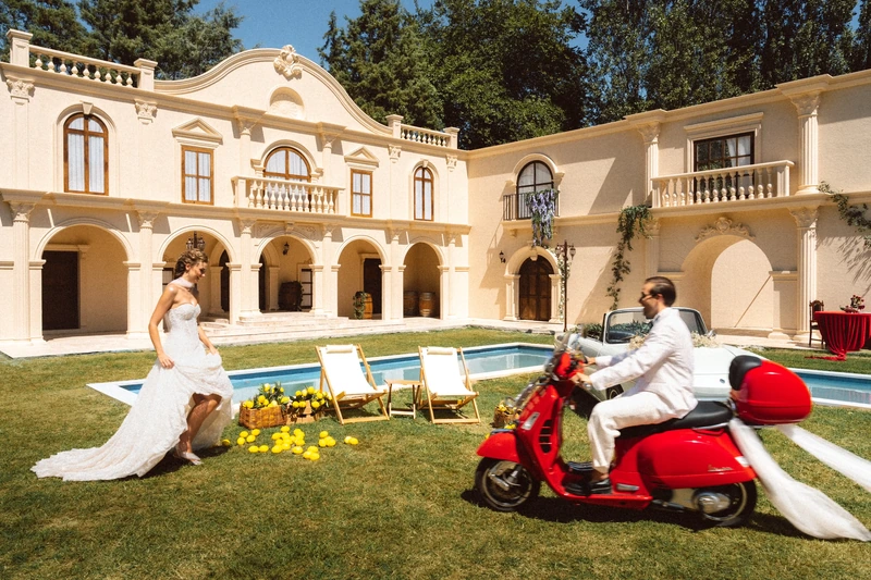 Çimde kırmızı Vespa ile çift; arkada köşk ve havuz