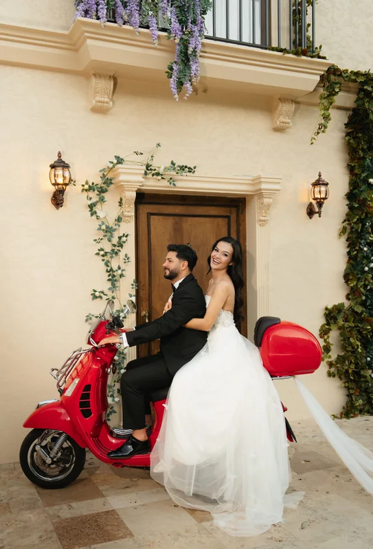 Köşk kapısının önünde kırmızı Vespa’nın yanında duran gelin ve damat